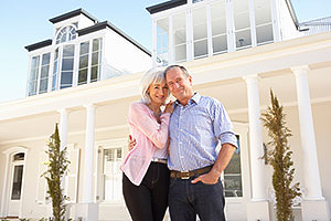 Mature couple standing in front of large home with many windows.